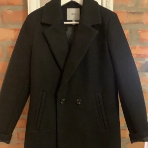 Svart Kappa ICHI  - Som ny så i jätte bra skick. Svart storlek 38. Slutar precis över knäna på mig som är 1.68 cm. Passar både för vinter/höst och vår.  Det ingår en tjock och gosig beige/benvit halsduk som är helt nytvättad.  Kan skickas eller hämtas upp. 