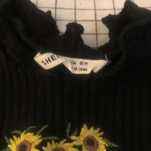 Långklänning - Svart , lång med solros detaljer! Lite korvat sytt på ärmar och botten av klänningen. Stretchigt material, lite ”randigt” tyg. strl 134 Fint skick, endast testad!