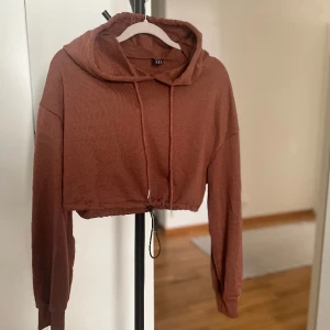 Croppad huvtröja rostfärgad tröja - Croppad huvtröja i en rostfärg. Man kan dra åt i midjan. Använd enstaka gång.
