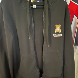 Moschino zip - Det är en Moschino zip tröja  Den har använts en del men är i ett bra skick 7/10 den är helt äkta köpt från Zalando för ett år sedan nypris för varan är 2500 och jag säljer den för ca 1/4 av priset. Helst mötas upp.