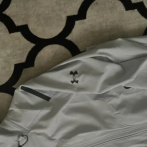 Under armour vit - En under armour vindjacka som är jätte fin och bekväm man kan ha på sig en tjock kofta under och så sitter den även jätte bra använd cirka 2-3 gånger jag har tagit hand om den jätte bra och inte smutsat den alls