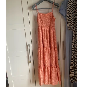 Långklänning - En långklänningen i en rosa/korall färg med vita blommor på från Na-kd! Nypris 399kr Endast använd 1 gång.  Så väldigt bra skick! 