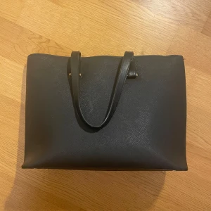 H&M väska -  Handväska med guldiga detaljer! Köpt för flera år sedan men inte använd särskilt mycket, plasten på handtagen har spruckit lite och knapparna på undersidan har tappat sin färg men annars i fint skick. Skicka om ni vill ha mått eller fler bilder!💗