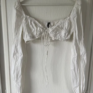 Supersöt vit topp - Otroligt söt vit långärmad topp. Oanvänd. Den är väldigt kort och det är därför jag aldrig har använt den. Knytdetalj där fram. 