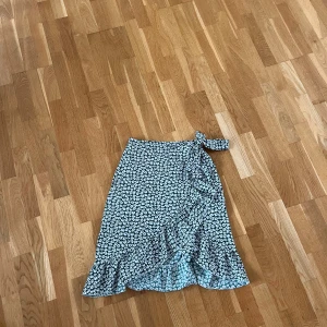 Kjol - Grön kjol med vita blommor. Kjolen är lite längre och går ner till knäna ungefär. Använd fåtal gånger därav fortfarande väldigt bra skick.