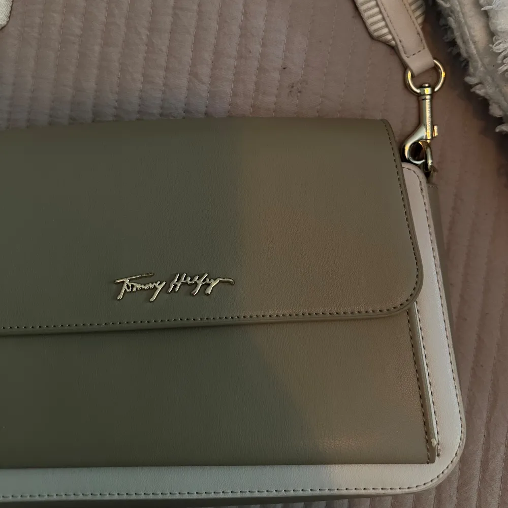 Liten axelremsväska som även går att ha som clutch från Tommy Hilfiger.  Beige med guldiga detaljer  Köpt för 170euro = cirka 1700kr . Väskor.