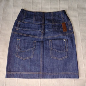 Blå högmidjad jeanskjol - storlek 32 - Blå högmidjad jeanskjol från Vero Moda. Modellen heter Brynja High Jeans Skirt Box. Skitsnygg med exempelvis en kort topp och stor jeansjacka. 99% bomull och 1% elastan. Storlek 32. Bara använd vid ett tillfälle och är så gott som ny. 