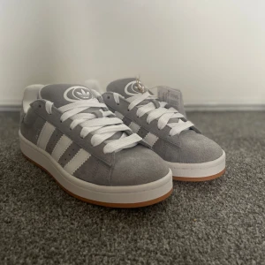 Gråa Adidas Campus 00s J - Ett par gråa Adidas Campus 00s J som är helt nya och säljs pga av fel storlek. Grå snören, låda och kvitto finns, skriv om det finns frågor.