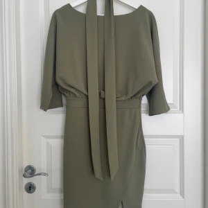Olivgrön klänning  - En oanvänd olivgrön klänning som kommer ner till knäna och uppåt. En vacker slits vid höger lår med halvöppen rygg, samt ett band att ha knutet runt midjan.