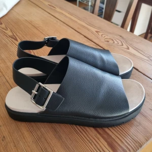 Svarta sandaler - Ett par fina sandaler i faux läder, alltså veganska. Har reglerbara spännen. Använda en gång, säljer då dom är för små för mig (är annars strl 38). Finns en liten repa på höger sko (bild 4). 
