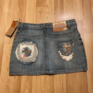 Jeanskjol från Rossena - En helt ny oanvänd, kort artsy jeanskjol från Rossena med unika broderade detaljer. Dekorerad med färgglada broderier och lappar på både fram- och baksidan. Extremt fin. 🤗 Midjemått: 38 cm, längd: 34cm.