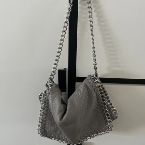 Grå Tiamo väska - Säljer min Tiamo Priscilla väska i storlek M! Kedjan är gjord kortare men det går att ta bort om man vill. Lite rostig på ett ställe annars fint skick🤍Nypris 550kr