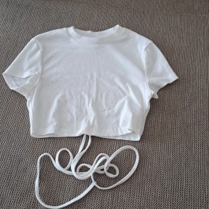 Vit ribbad croppad topp - En vit ribbad croppad topp med korta ärmar och rund hals. Toppen har en knytning i midjan för en justerbar passform.