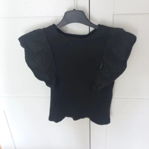Svart topp med volangärm - Säljer svart topp med volangärm från  kappahl i storlek 146/152 men passar typ som en XXS. Använd 1-2 gånger.