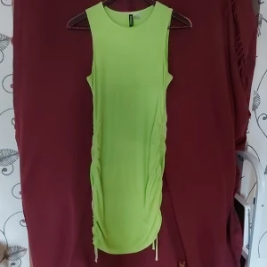 Slimmad neongrön klänning - Neonfärgad slimmad långklänning med band på sidorna som går att dra åt. Smal passform men stretchig. Bra skick
