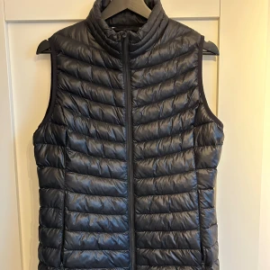 Svart dunväst - Säljer denna svarta dunväst som är perfekt till våren/sommaren. Nyskick!! Inga defekter!! Två fickor fram och cirka 60cm lång. Nypris 599kr.