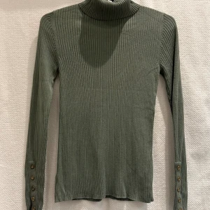 Grön polojumper - Grön stretchig polojumper med dekorativa knappar på ärmarna.   Strl: 8