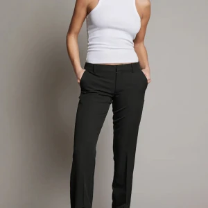 VERA KOSTYMBYXA MED LÅG MIDJA - Svarta lågmidjande kostymbyxor, använd ett fåtal gånger. Storlek 36 petit med slits. Vill köpa exakt likadana,mindre storlek just därför säljer jag dem.