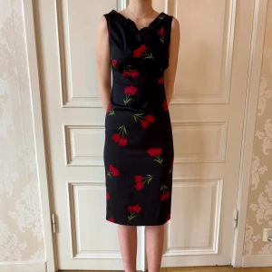 Svart blommig klänning, Stop Staring! - Jättefin svart klänning med röda blommor. Storlek M. Liten rosett på ryggen. Modellen på bilden är 173 cm och har storlek 38 i de flesta andra kläder. Aldrig använd. Vi har lagt ner vår klänningsbutik och säljer ut. Ny pris är 2000-3000kr