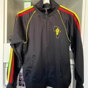 AFRIKAAAAAA ZIP - asfet zippup med adidas ish ränder i rastaaaah colorway men de inte adidas okk! sitter som en S tts ksk ens xs på vissa💯💚💛❤️ PS: Rädda Kongo - stöd via röda korset eller privata aktörer NU💔