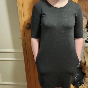 Klänning med trekvarts ärm - Grå klänning lite tjockare material typ joggingtyg. Fickor på sidorna. Jättebra skick. Storlek S men passar M med beroende på hur man vill att den ska sitta. Tjejen på bilden använder S i vanliga fall.