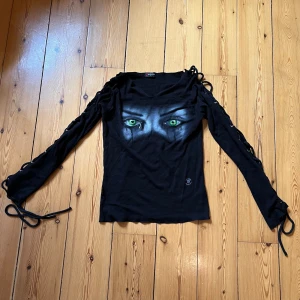 Alt tröja med snörning - Jättefin och unik långärmad topp från Spiral Direct i stl L (true to size, lite stretchig). Lång snörning längst ärmarna. Grafik med gröna ögon i mitten. Använd men fint skick! Inga bilder på 🖤