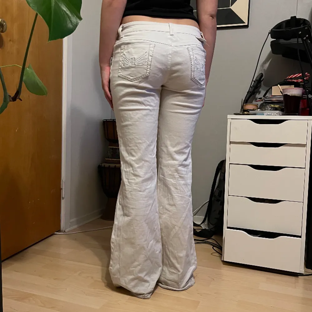 Lågmidjade vita utsvängda byxor med broderade vingar på fickorna ! 💕 -midjemått rakt över= 41cm -innerbenslängd= 82cm -längd på hela byxorna= 104cm. Jeans & Byxor.