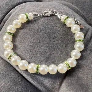 Handgjort pärlarmband med vita pärlor, gröna  glittrande mellanplattor och silvrigt spänne. Justerbar passform mellan 19-24 cm.💕