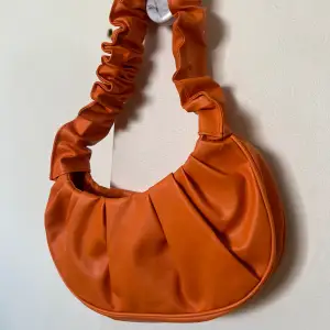 En orange handväska som går att stänga till med en knapp. 