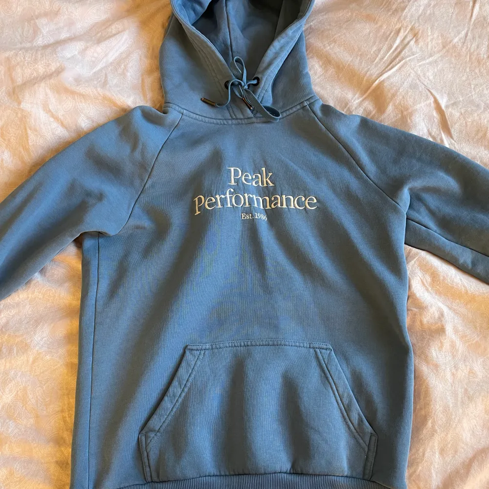 Mycket fin blå hoodie från Peak Performance. Den är använd men är i fint skick. Något liten i storleken. Nypris 1200.. Hoodies.