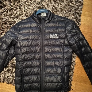 EA7 Jacka - En mörkblå EA7 jacka i Bra skick, 8/10 ungefär, inte använt på 2 år och jag säljer till ett bra pris då jag bara vill få bort den! S men passar för M! 