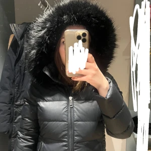 Tommy Hilfiger dunjacka  - Svart dunjacka från Tommy Hilfiger i storlek M/38. Den är svart med avtagbar fuskpäls utan att det syns att man tagit av den. Jättefräsch inga anmärkningar, använd sparsamt av min mamma. Går att knäppa upp nerifrån. Säljs pga att har andra dunjackor.