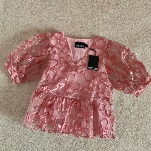 Pieces rosa metallisk blus med ballongärmar - Otroligt vacker blus från Pieces i rosa metalliska blommönster. Aldrig använd, ny med tags kvar. Storlek XS men passar även S utan problem.
