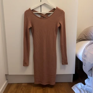 Ribbad klänning - Klänning med korsande band på ryggen. Färgen är typ brun, rosa, beige. En djup mauve färg. 
