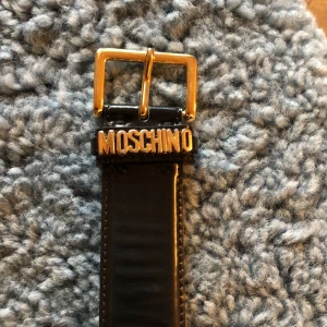 Moschino skärp, bälte. Buy a  patent leather belt. Lackläder. - Supersnyggt svart läderbälte, sparsamt använt. (Nypris:  315 EURO/SEK 4000).    Längd från spänne till slutände:90 cm, men längd från spänne till första skärphål: 75 cm. Bredd: ca 3,3-3,5 cm Det plickpris: 1500 SEK