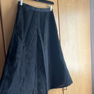  A formad svart Långkjol - A formad lång kjol i svart paisley vävd tyd, bra kvalite knappt använd. Dragkedja på baksidan, vadlångt 