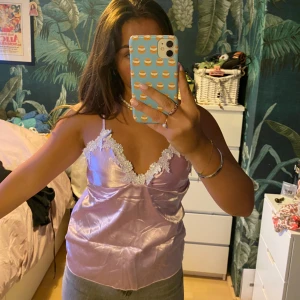 Lila ”satintopp” - Söt lila topp i ”satin” med vit spetsdetalj.  Står ingen storlek men skulle säga att det är som 36 ungefär. Styvt i tyget, så inte så mycket mer än Bkupa som får plats :)  OBS ena plastringen i bak har gått sönder, se bild 3, så den måste lagas. 