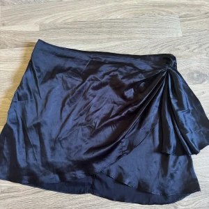 Svart kjol från Shein - En elegant svart kjol från Shein i storlek 3XL. Kjolen har en omlott-design och är tillverkad av polyester och elastan, vilket ger den en glansig finish och en bekväm passform. Kjolen har en dragkedja baktill för enkel på- och avtagning. Använd en gång.
