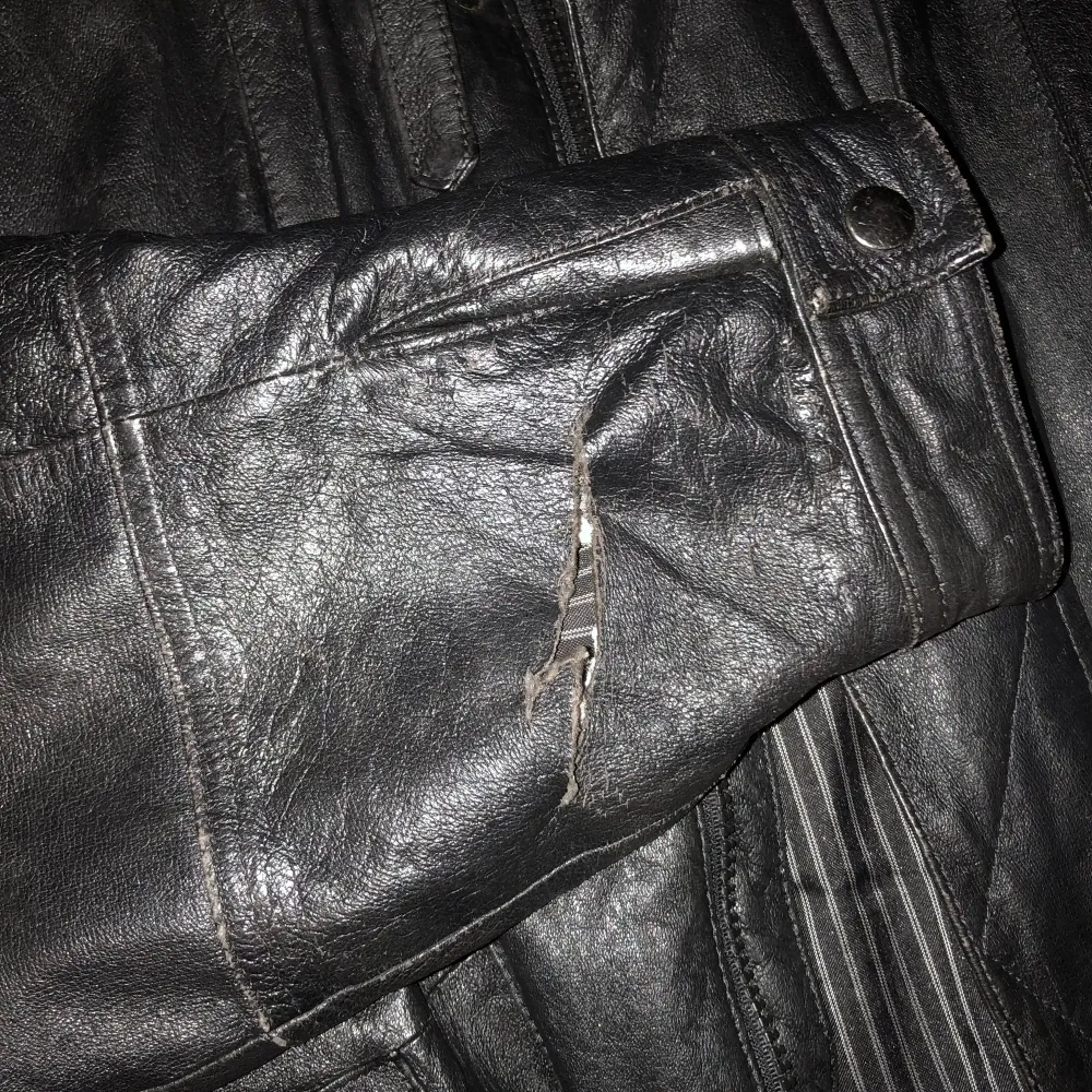 En svart skinnjacka med långa ärmar och två stora fickor framtill. Den är i välanvänt skick med en reva på ena ärmen. Strl 54 aka väldigt stor o baggy :) 100% äkta läder, om du vill ha fler bilder eller frågor skriv bara <3. Takit.