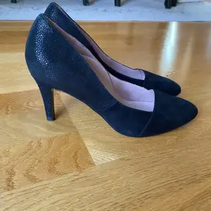 Eleganta svarta pumps från Tamaris med spetsig tå och klack. Skorna har en subtil glittrig yta och är i mycket bra skick då de endast varit använda vid ett tillfälle. 