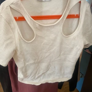 Beige ribbad topp - En beige ribbad topp med korta ärmar och unika utskärningar vid axlarna. Toppen är croppad och har en tight passform.