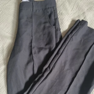 Svarta kostymbyxor  - Svarta kostymbyxor med veck på sidorna, från madlady. Kedja framtill för att stänga byxorna. 