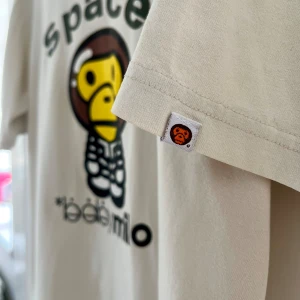 Beige t-shirt från Baby Milo - Vintage t-shirt Baby Milo Köpt på 90-talet i New York åt min äldsta son                                          Färg; Beige, Str: M (liten i str), Anmärkning: Litet hål nedre söm på baksidan, samt ett streck (ev fr en penna) på framsidan, se foton 