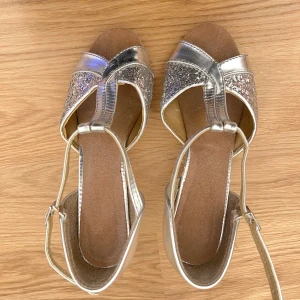 Dansskor silver med mockasula - Dansskor med mockasula. 7 cm klack, silver och silver glitter framtill. Är en skönhet på fötterna. Sköna att dansa med. Lite slitage på klacken som knappt märks.  