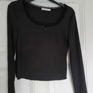 Svart topp spets - Svart topp med spets och liten rosett framtill. 