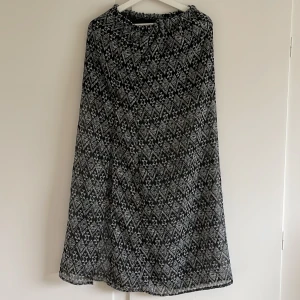 Svart och vit mönstrad långkjol - Säljer en superfin svart och vit långkjol med ett coolt geometriskt mönster. Kjolen har en elastisk midja för extra komfort och är perfekt för både vardag och fest. Materialet känns lätt och luftigt, vilket gör den idealisk för vår och sommar. Passar perfekt med en enkel topp och sandaler eller sneakers.