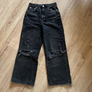Svarta jeans från gina tricot - Säljer ett par svarta jeans från gina tricot i storlek 36. De är i en cool, sliten stil med hål på knäna och fransiga kanter. Jeansen har en hög midja och en wide fit, vilket gör dem både bekväma och trendiga. Perfekta för en avslappnad vardagslook!
