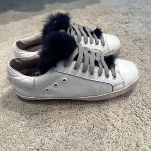 Vita sneakers med svart pälsdetalj - Säljer ett par goldengoose  med en unik svart pälsdetalj på snörningen. Skorna är i skinn och har en klassisk design med perforerade detaljer på sidorna. nypris ligger runt 6800kr! vårat pris 1499kr 