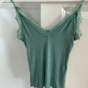 Grön ribbad linnetopp med spetsdetaljer - Säljer en superfin grön ribbad linnetopp med spetsdetaljer runt halsen och ärmarna. Perfekt för sommaren eller en festlig kväll. Toppen är i bra skick och väldigt bekväm att ha på sig. Passar perfekt till både jeans och kjol!