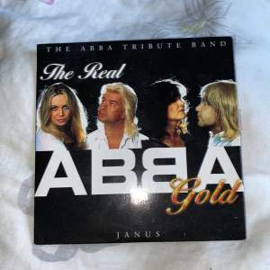 Säljer en CD med titeln 'The Real ABBA Gold' av The ABBA Tribute Band. CD:n innehåller 14 klassiska ABBA-låtar som 'Dancing Queen', 'Super Trouper', 'Chiquitita', och 'Waterloo'. + mer. Skivan är i bra skick och kommer med originalfodralet. Perfekt för alla ABBA-fans som vill njuta av deras tidlösa hits!